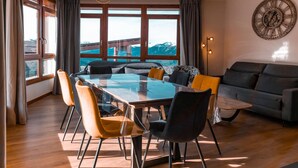 A modern dining area with a glass table and chairs, a sofa, and a large window with a mountain view. - 3-room apartment with balcony, WIFI, parking and pool access, Les Arcs 1800 (Les Arcs 1800)