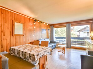 Ein Zimmer mit einer Holzwand, einem Esstisch mit gemustertem Tischläufer, einer Couch und einem kleinen runden Tisch.