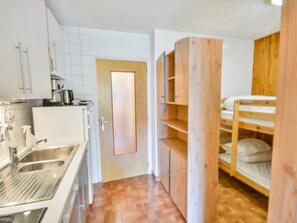 A compact kitchen with a sink, cabinets, and a stove. There is a door with a window, and a bunk bed with wooden headboards. - Studio in Morzine center, 4 pers, balcony, WIFI (Morzine)
