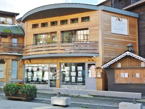 A wooden building with a balcony, a sign for 'Agence Olivier 1952', and a flower planter in front.