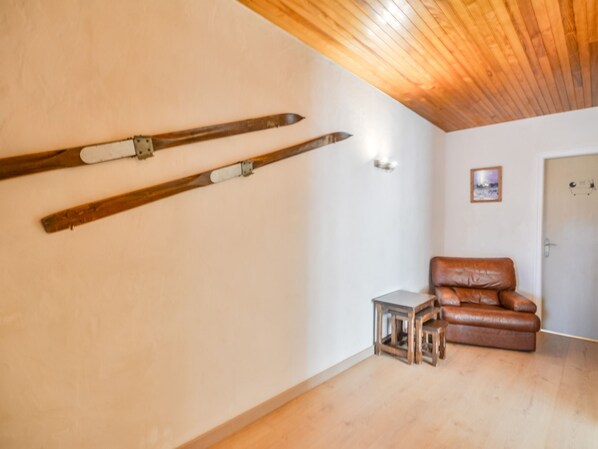 Une pièce avec un plancher en bois, un canapé en cuir marron et deux paires de skis accrochées au mur.