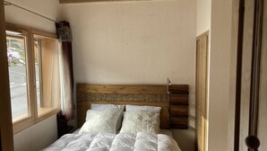 Una camera da letto con una testiera in legno, un letto con biancheria da letto bianca, una finestra con tende e vista su una strada.