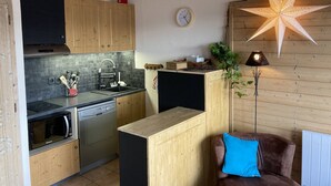 Una cucina compatta con mobili in legno, un forno a microonde e un lavello. Si vede un orologio appeso al muro e un lampadario a forma di stella.