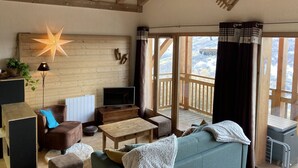 Un accogliente soggiorno con soffitto in legno, una lampada a forma di stella, un televisore e una grande finestra con tende.