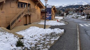 Un chalet in legno con una scala che conduce a un balcone, un lampione e una vista sulle montagne innevate sullo sfondo.