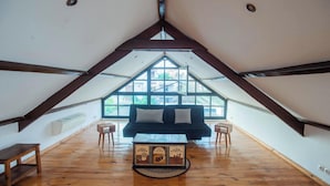 Ein Loft-Zimmer mit geneigter Decke, einer schwarzen Couch, einem Holztisch und einem großen Fenster für natürliches Licht.