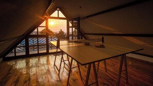 Ein Zimmer mit Holztisch und Blick auf den Sonnenuntergang durch ein großes Fenster.