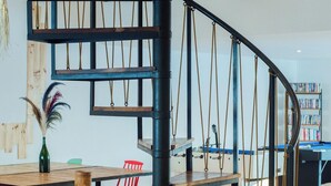 Eine Wendeltreppe mit Holzvertäfelung und Metallgeländern, ein Holztisch mit Stühlen und ein Bücherregal im Hintergrund.