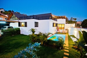 A modern house with a swimming pool, surrounded by well-maintained lawn and tropical plants.