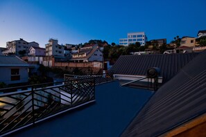 A rooftop terrace with a metal railing, a view of residential buildings, and a clear sky.