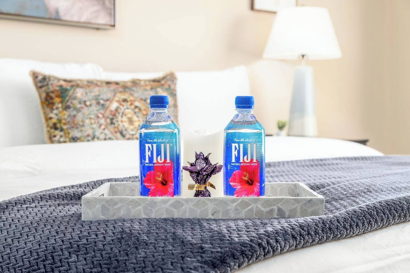Sängyllä on kaksi pulloa Fiji-mineraalivettä ja koriste-esine tarjottimella.