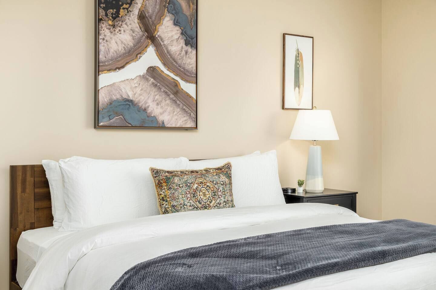 Habitación de hotel con una cama, una mesita de noche con lámpara y dos obras de arte colgadas en la pared.