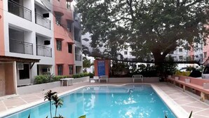 Une piscine rectangulaire entourée d’une terrasse carrelée, avec un grand arbre au centre.