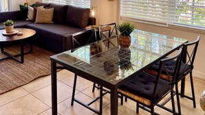 A modern living room with a glass dining table, dark sofas, and a hanging light fixture. - 260D - Boca Retreat w/ Pool, Parking, Near Evert Tennis & Shops (Boca Raton)