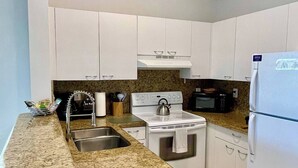 A kitchen with white cabinets, a granite countertop, a stove, a microwave, and a refrigerator. - 260D - Boca Retreat w/ Pool, Parking, Near Evert Tennis & Shops (Boca Raton)