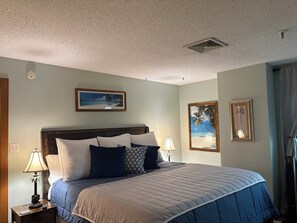 A bedroom with a bed, a nightstand, a lamp, and two framed pictures on the wall. - Grand Lake Getaway – Vista Towers 10th Floor Condo with Golf & Lake Views (Monkey Island)