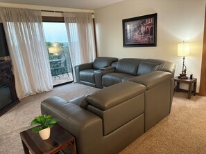 A living room with a sectional sofa, a small table with a plant, a lamp, and a framed picture on the wall. - Grand Lake Getaway – Vista Towers 10th Floor Condo with Golf & Lake Views (Monkey Island)