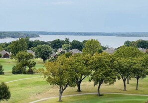 Ein Golfplatz mit Häusern im Hintergrund und einem Gewässer in der Ferne.