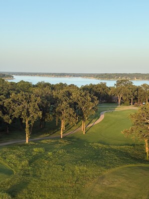 A golf course with a water body in the background, surrounded by trees. - Grand Lake Getaway – Vista Towers 10th Floor Condo with Golf & Lake Views (Monkey Island)