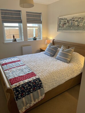 A neatly made bed with a quilt, two bedside tables, a lamp, and a painting on the wall. - Beautiful coastal apartment (Cellardyke)