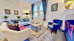 A living room with a sofa, armchair, coffee table, and a chessboard. There are windows with curtains, a radiator, and a lamp. - Funky 2 Bed Apartment in the Heart of Historic Rochester (Rochester)