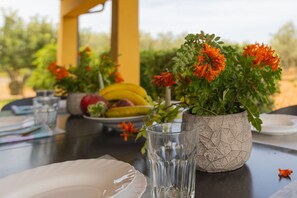 A dining table with a clear glass, a white plate, and a potted plant with orange flowers. - Finca SON SERRA, house for 4, with pool near Buger (IB)
