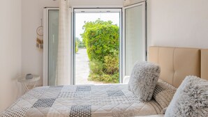 Een slaapkamer met een groot bed, uitzicht op een tuin door een glazen deur en een klein nachtkastje.