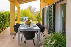 An outdoor patio with a table set for dining, surrounded by chairs, potted plants, and a small playhouse in the background. - Finca SON SERRA, house for 4, with pool near Buger (IB)