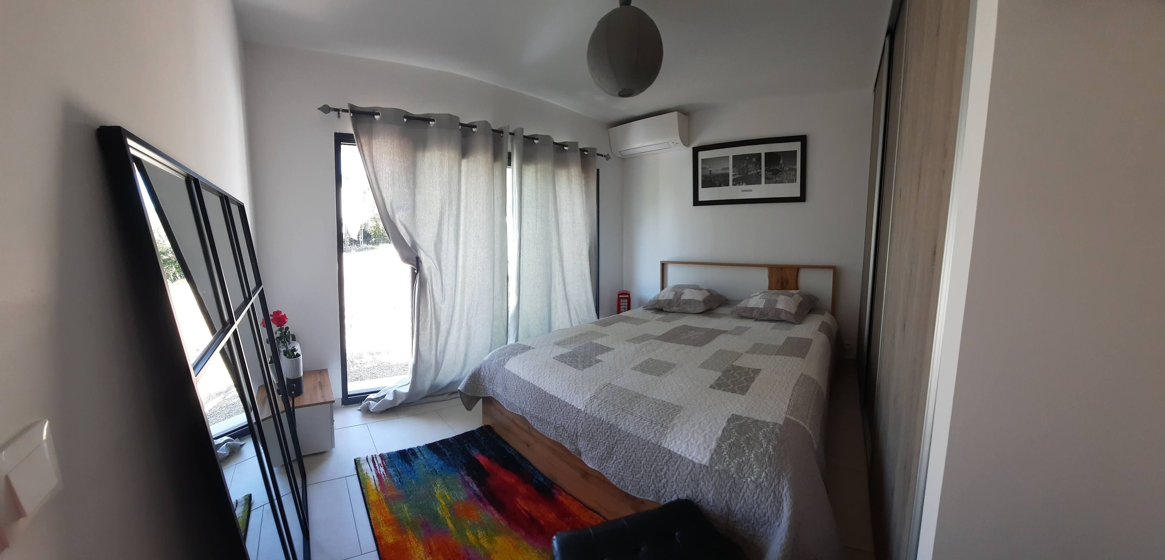 Quarto com cama, mesa de cabeceira, cortinas na janela e ar condicionado fixado na parede.