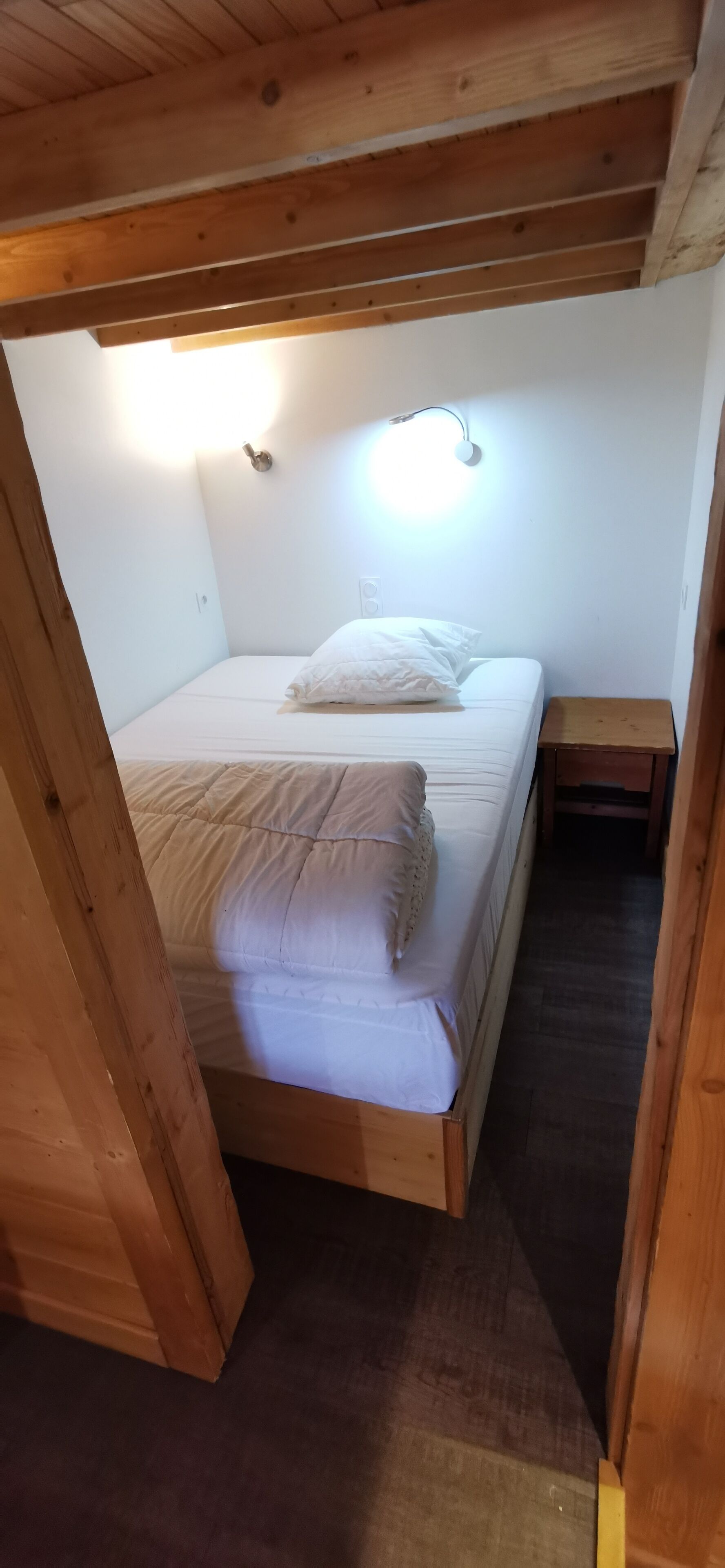 Una habitación pequeña y acogedora con una cama individual, una mesita de noche y techo de madera.