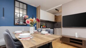 Un comedor moderno con una mesa de madera preparada para cuatro personas, un jarrón de flores y un televisor de pantalla plana grande montado en la pared.