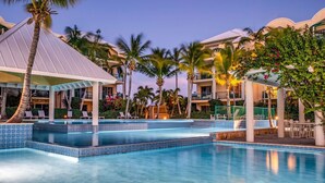 Un hotel con piscina, palmeras y una zona de estar techada.