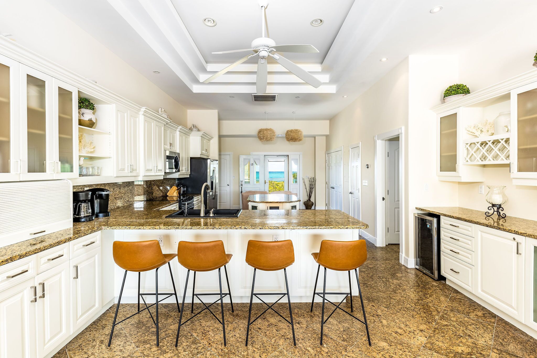 A modern kitchen with white cabinetry, a granite countertop, and a central island with bar stools.