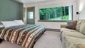 Une chambre avec un lit, un canapé, une fenêtre donnant sur des arbres et une porte.