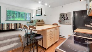Un espace de vie compact comprenant un coin cuisine, un coin repas, un canapé et une vue sur la forêt.