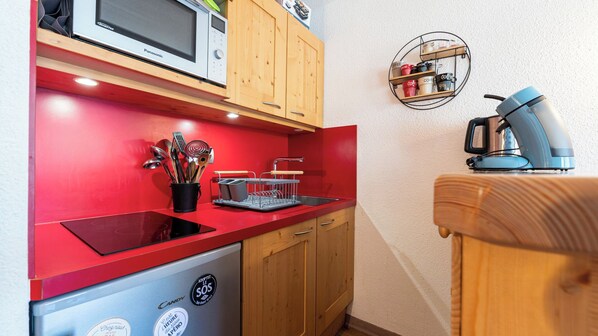 Une cuisine compacte avec un plan de travail rouge, un four à micro-ondes, une machine à café et des placards en bois.