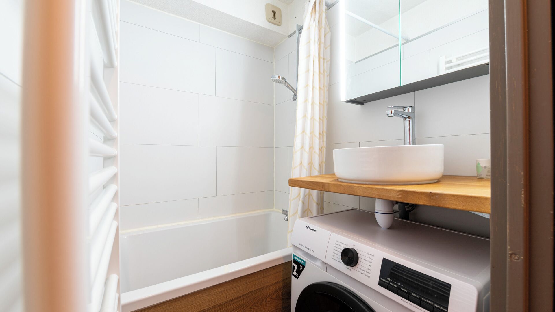 Une petite salle de bain avec une douche, un lavabo posé sur une étagère en bois et un lave-linge.