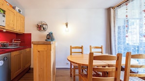 Una cuina compacta amb armaris de fusta, un taulell vermell i una cafetera. Hi ha una zona de menjador amb una taula i cadires de fusta.