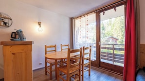 Taula de dinar de fusta amb cadires, màquina de cafè i llum penjada a la paret en una habitació amb terra de fusta i una porta corredissa de vidre que dona a zona exterior.