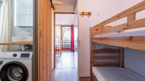 Habitació d'hotel senzilla amb rentadora, lliteres de fusta, una taula petita i vista a través d'una porta de vidre.
