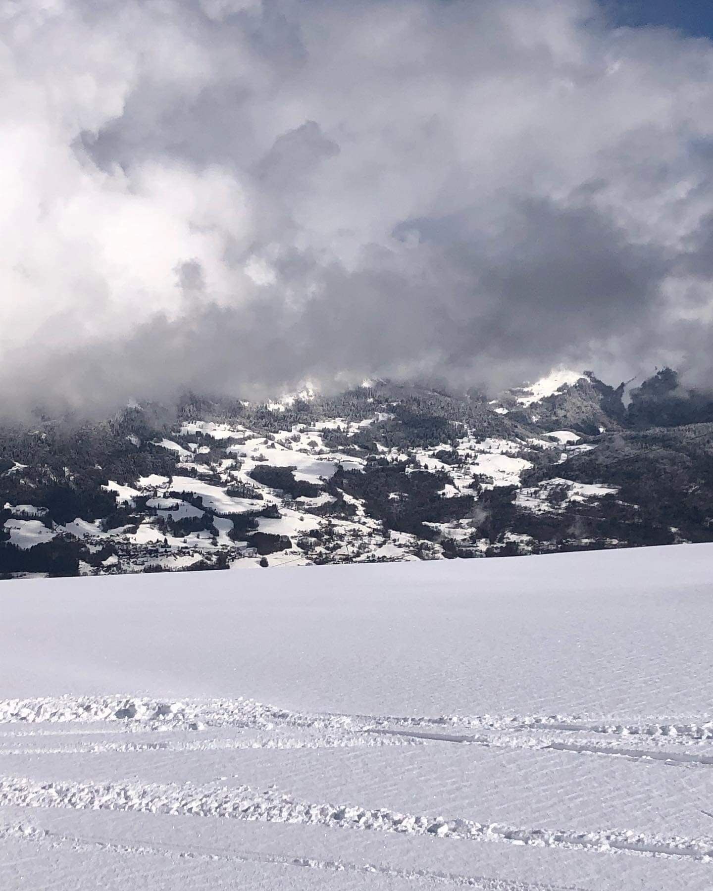 A snowy landscape with a flat, open area in the foreground and a mountainous backdrop.