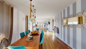 Een ruime eethoek met een lange houten tafel, teal stoelen en een fruitmand in het midden.
