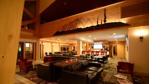 Un hall d’entrée spacieux avec des sièges en cuir, un plafond en bois orné de motifs de montagnes et un grand écran de télévision.