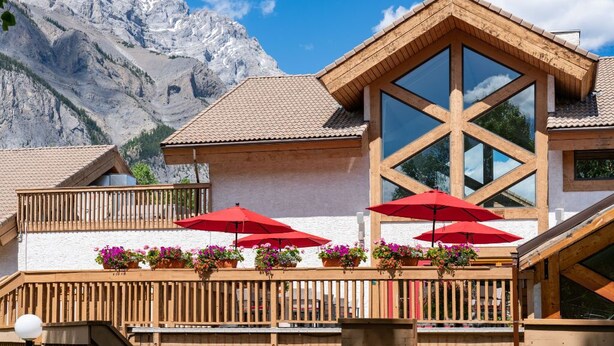 Un chalet doté d’un balcon en bois, de parasols rouges et de jardinières fleuries.