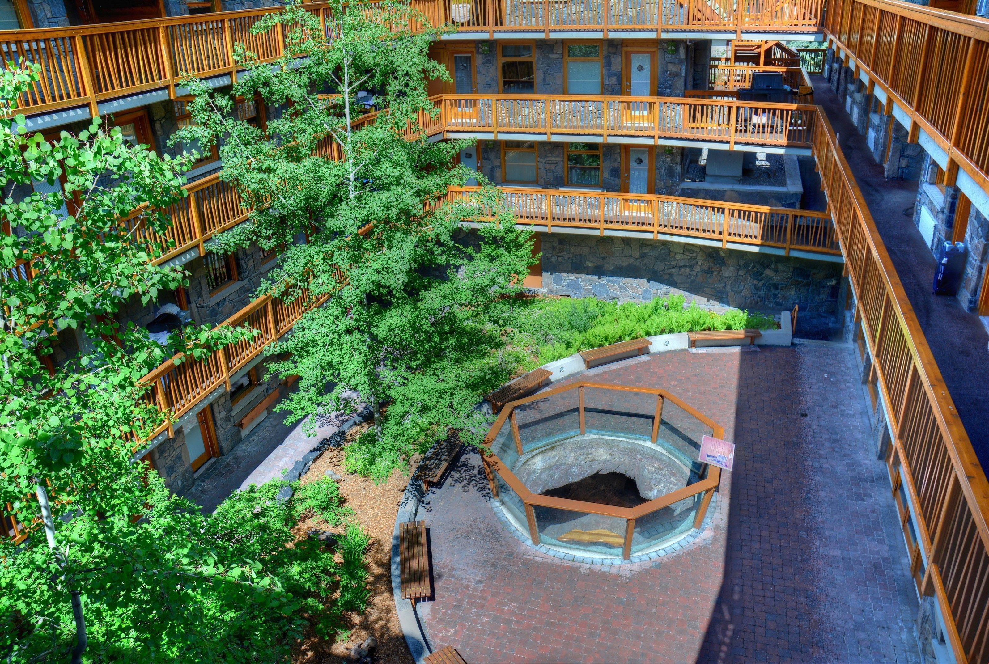 Een hotel met meerdere verdiepingen, houten balkons, een centrale binnentuin met een ronde zithoek en weelderige begroeiing.