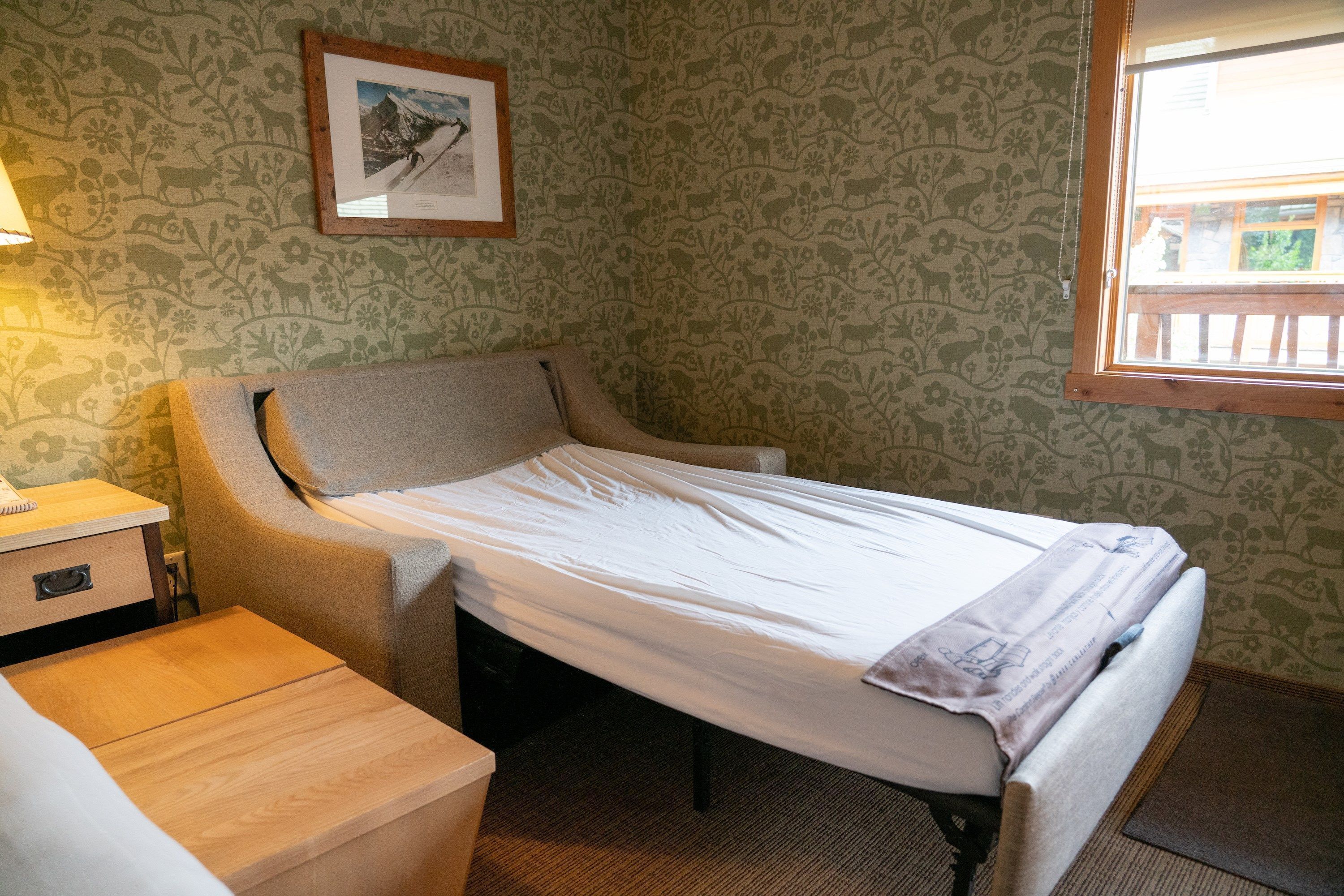 A single bed with a wooden frame, a bedside table, and a lamp.