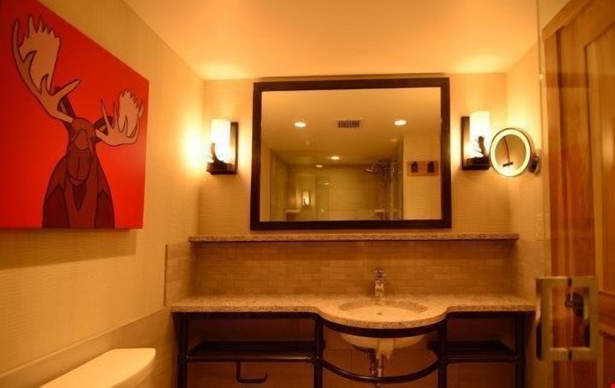 Une salle de bain avec un grand miroir, deux lavabos et des toilettes.