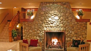 A stone fireplace with a fire, surrounded by a sofa and chairs, in a room with a wooden staircase and potted plants. - Loft with Private Jetted Tub/Access to Spa (Banff)