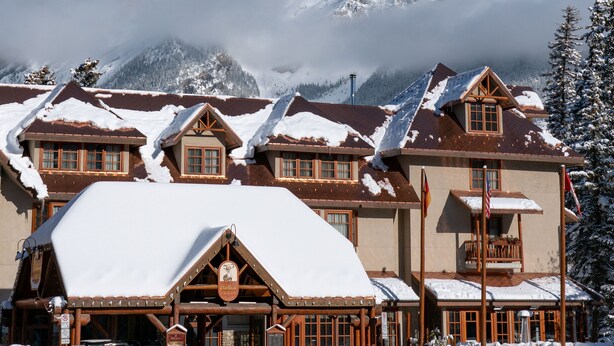 A lodge with a snow-covered roof and a mountain backdrop. - Accessible room, Central Banff, Hot Pool! (Banff)