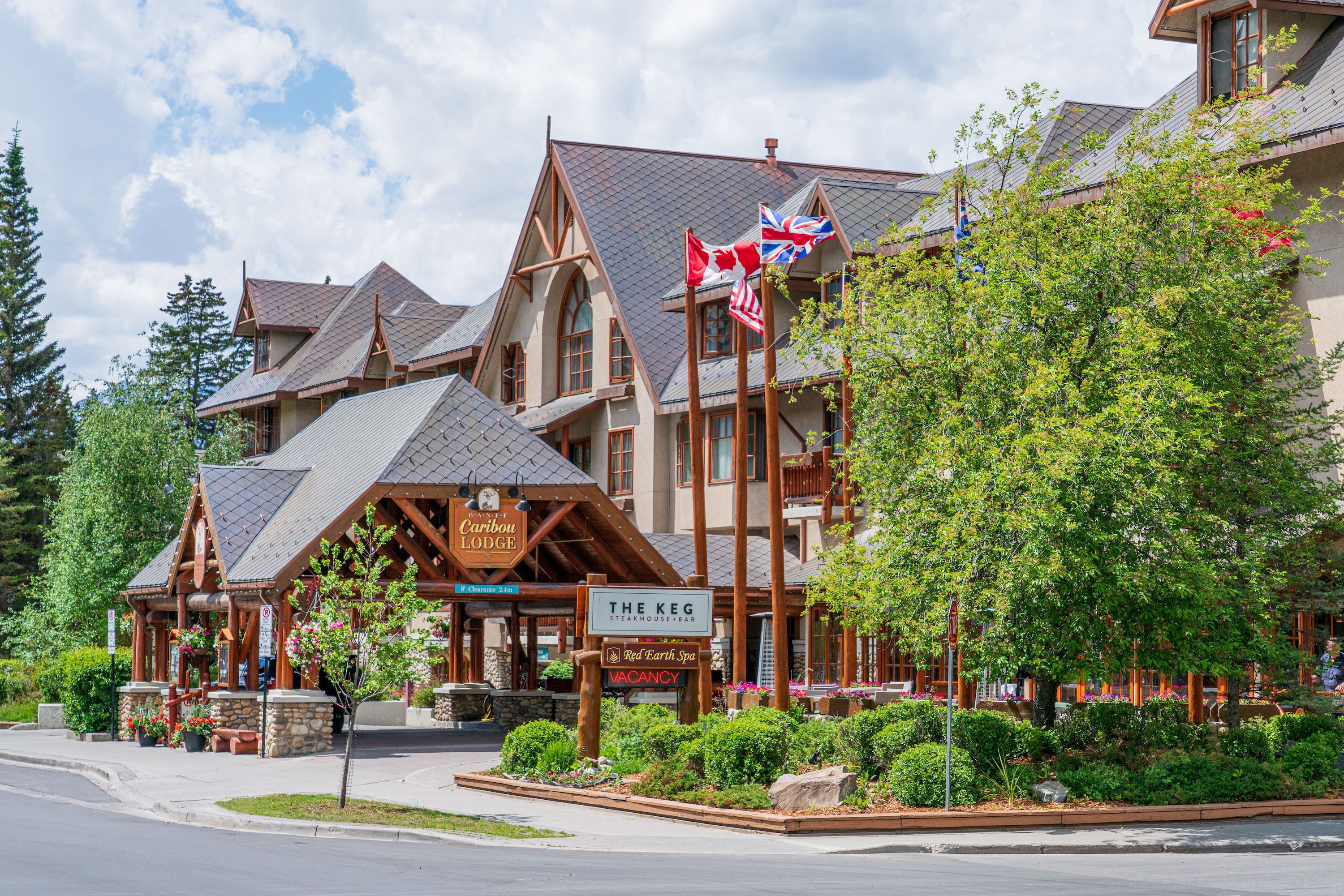A lodge with a sign for The Keg Steakhouse Bar and Red Earth Spa, surrounded by lush greenery and a clear sky.